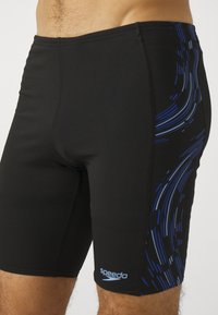 Fekete úszónadrág rugalmas anyagból, kék absztrakt mintákkal az oldalán és sima textúrával. Speedo logó a lábszáron.