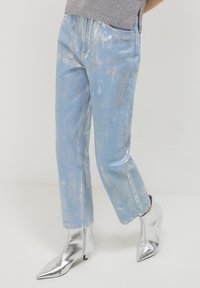 Jeans in denim azzurro chiaro con una finitura lucida, caratterizzati da un taglio dritto e dettagli leggermente strappati. Abbinati a stivaletti metallici argento alla caviglia.