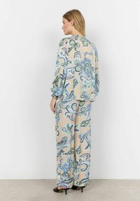 Costum bej deschis cu un model paisley în verde și albastru. Mâneci lungi și pantaloni largi cu o croială lejeră. Textură fină, strălucire subtilă.