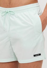 Mentazöld úszóshort könnyű anyagból, rugalmas derékkal, zsinóros részlettel és egy kis fekete Calvin Klein logóval.