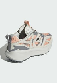 Grå och persikofärgade sportskor med en strukturerad ovandel, meshnätpaneler och en tjock vit sula. Har en dragflik och mönstrade detaljer.