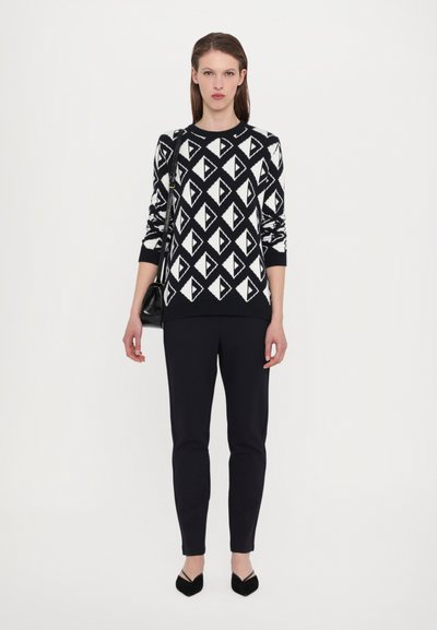 Strikket svart og hvit genser med et geometrisk trekantmønster, kombinert med svarte slim-fit bukser og spisse hæler.
