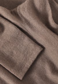 Smeđi pleteni materijal s mekim teksturom, s preklapajućim slojevima i glatkom završnom obradom, ističući lagani i udobni materijal.