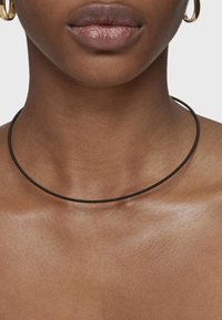 Collar choker negro hecho de un material flexible, con un diseño liso y esbelto que se ajusta cerca del cuello.