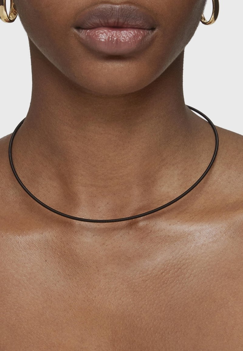 Collar choker negro hecho de un material flexible, con un diseño liso y esbelto que se ajusta cerca del cuello.