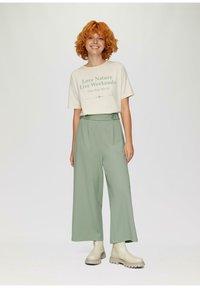 Beige katoenen t-shirt met groene tekst, gecombineerd met lichtgroene wijde broekspijpen met zijknopen. Tan enkellaarsjes met dikke zolen.