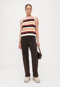 Canottiera a righe in maglia con colori arancione, nero e crema, abbinata a jeans larghi marrone scuro e sneakers chunky beige. Borsa marrone.