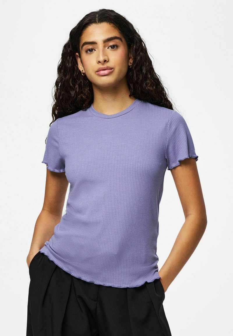 T-shirt violet côtelé avec manches courtes à volants et encolure ronde, présentant une coupe ajustée et une texture douce. Associé à un pantalon foncé.