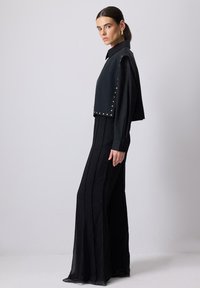 Sort outfit med en struktureret top med en rund krave og guldfarvede nitter, parret med en flydende, plisseret maxiskirt.
