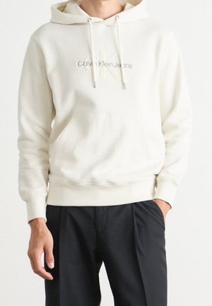 Sudadera color crema con cordones, bolsillo frontal y logo bordado de "Calvin Klein Jeans". Cuenta con puños y dobladillo acanalados.