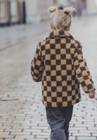 Bruine en beige geruite fleecejas met een kraag, lange mouwen en een pluche textuur. Draag het met donkere broek terwijl je over kinderkopjes loopt.