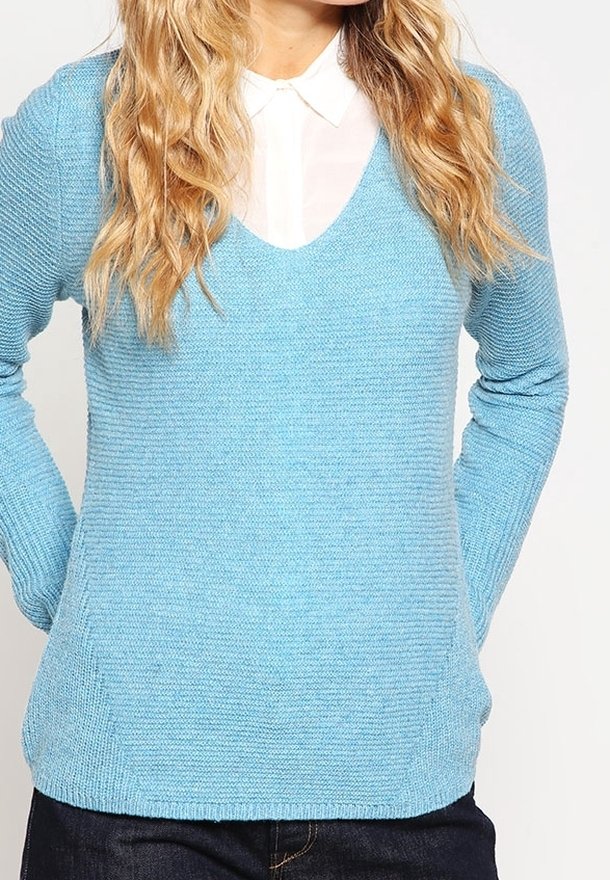 Suéter de punto azul claro con escote en V, textura acanalada y mangas largas. Combinado con una camisa blanca de cuello debajo.