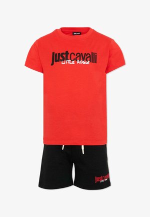 Maglietta rossa a maniche corte con la scritta "Just Cavalli Little Rogue" in bianco e nero, abbinata a pantaloncini neri con scritte rosse e bianche abbinate.