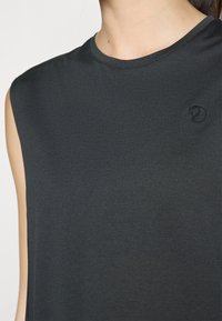 Ermeløs mørkegrå topp i teksturert stoff, har rund halslinning og en liten brodert logo på brystet.