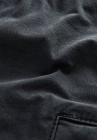 Primo piano di tessuto nero spiegazzato con cuciture visibili vicino al bordo inferiore, che mostra la trama e i dettagli del materiale.