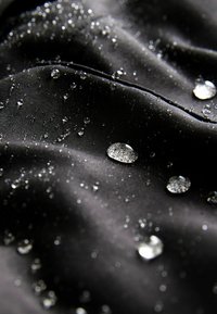 Tissu noir imperméable au toucher lisse, présentant des gouttes d'eau à sa surface, réfléchissant la lumière de différentes tailles.