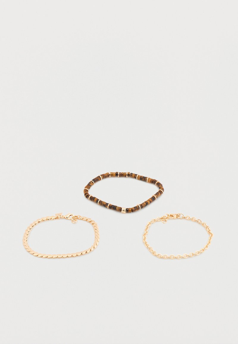 Trois bracelets sur une surface unie : un bracelet marron en perles, une chaîne en or à maillons plats, et une chaîne en or à maillons arrondis.