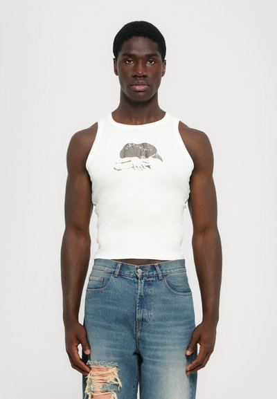 Weißes Baumwoll-Top mit Grafikdesign auf der Vorderseite. Kombiniert mit zerrissenen blauen Jeans im Denim-Stil, die ausgefranste Kanten und eine helle Waschung aufweisen.