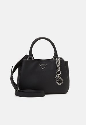 Sac à main Guess en cuir noir avec poignées courtes, bandoulière amovible et pendentif logo argenté suspendu sur le côté avant.