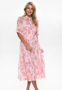 Bloemenmidi-jurk in doorschijnende roze stof. Voorzien van een knoopsluiting aan de voorkant, korte mouwen en een ceintuur in de taille. Versierd met kleurrijke bloemenpatronen.