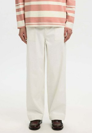 Personne portant un pantalon blanc à jambes larges avec des poches plaquées, un haut à manches longues rayé rose et blanc, ainsi que des chaussures marron foncé.