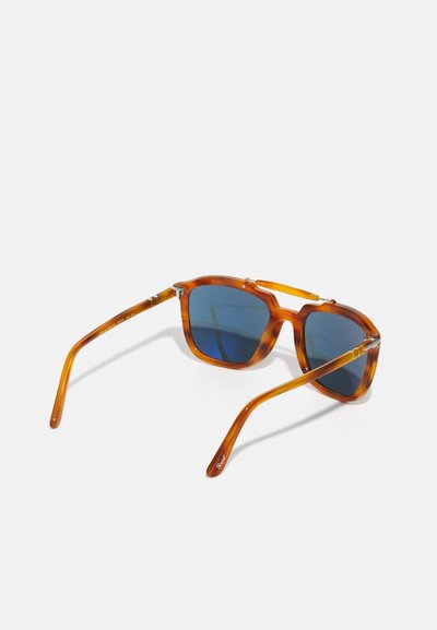 Ochelari de soare pătrați cu un cadru translucid de culoare chihlimbar și lentile de un albastru închis. Au brațe subțiri cu un detaliu subtil de brand.