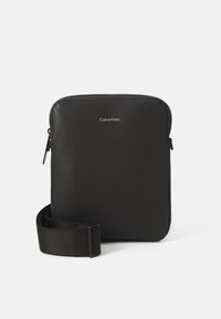 Svart axelväska i strukturerat syntetmaterial. Har en dragkedjestängning och justerbar rem. Litet logotyp på framsidan. Fyrkantig form.