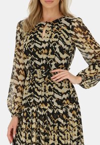 Długo-sługawna sukienka z przezroczystego materiału, z czarnym, beżowym i złotym abstrakcyjnym wzorem, dekoltem w kształcie łezki, cinchowaną talią oraz detalami w plisowanej spódnicy.