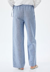 Lichtblauwe, wijde broek met een geweven textuur. Voorzien van een elastische tailleband met een trekkoord. Strakke boorden en minimale details.