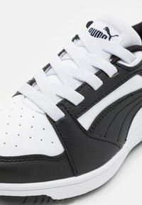 Black and white athletic shoe featuring a textured leather upper, perforated toe, white laces, and a contrasting logo on the tongue.