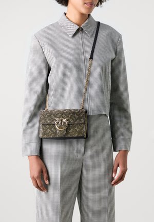 Piccola borsa rettangolare con un motivo ornato in oro e nero, caratterizzata da un accento metallico circolare e una tracolla a catena, indossata a tracolla.