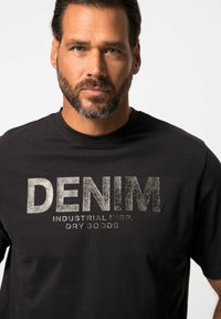 Zwarte katoen t-shirt met een zilveren verouderd tekstontwerp met de tekst "DENIM" en "INDUSTRIAL INSP. DRY GOODS" op de voorkant. Rond de hals.