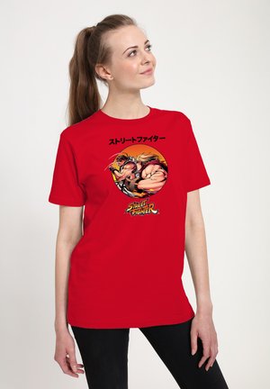 Kvinde iført rød t-shirt med Street Fighter-figurerne Ryu og Ken i kampstilling og japansk tekst over dem.