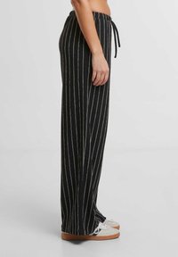 Černo-bílé pruhované kalhoty s širokými nohavicemi a stahovacími šňůrkami v pase, vyrobené z texturované látky, s rozparky na lemu.