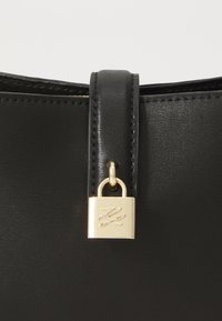 Sac à main en cuir noir avec un imposant fermoir en forme de cadenas doré et une bandoulière assortie. Texture lisse avec des détails de couture précis.