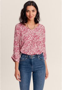 Rot-weiße gemusterte Bluse mit V-Ausschnitt und Dreiviertelärmeln, kombiniert mit hochgeschnittenen blauen Jeans. Glatte Stoffstruktur.