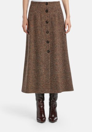 Brązowa spódnica midi z tweedu z guzikami z przodu, zestawiona z ciemnobrązowymi botkami na obcasie o wzorze krokodyla na białym tle.