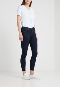 Vit kortärmad t-shirt med blå tie-dye detaljer, tillsammans med mörkblå åtsittande jeans och vita sneakers. Enkelt design, mjuk textur.