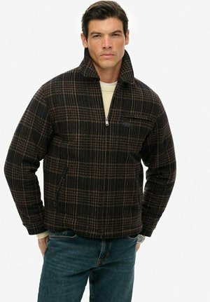 Chaqueta de cuadros en tonos oscuros con un cuello alto, que cuenta con un cierre frontal con cremallera, bolsillos laterales y un sutil logotipo en el pecho. Tela texturizada.