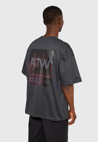 Szara, oversize koszulka z bawełny, z nadrukiem graficznym na plecach zawierającym tekst i abstrakcyjne wzory w ciemnych odcieniach.