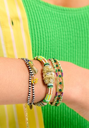 Bracelets assortis : rayés noir et blanc, perles vertes et blanches, accents dorés, motifs colorés, textures variées, superposés sur un poignet.