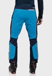 Niebieskie i granatowe spodnie narciarskie z zamkami błyskawicznymi, wyposażone w technologię RECCO. Gładka faktura, ergonomiczny design i kolorowe akcenty.