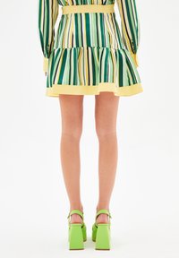 Vestido a rayas con colores verde, amarillo y azul marino, con un dobladillo con volantes y una banda amarilla. Sandalias verdes de tacón ancho completan el conjunto.