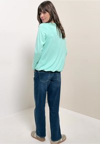 Helles Mint longärmliges Oberteil mit lockerer Passform, kombiniert mit dunkelblauen geraden Jeans. Die Rückansicht zeigt ein einfaches Design und eine weiche Textur.