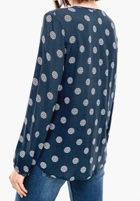 Navy blue long-sleeve blouse with white circular pattern, made from a smooth fabric. Features a round neckline and buttoned cuffs.