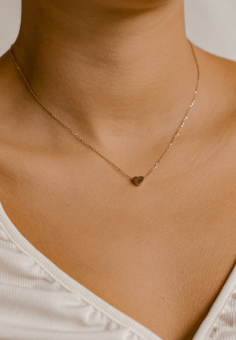 Collana in oro con un piccolo ciondolo a forma di cuore, che mette in evidenza una finitura liscia e link delicati sul tono della pelle.