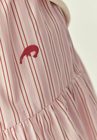 Tissu rayé verticalement rose et blanc avec de fines lignes rouges, avec une petite figure d'animal rouge brodée.