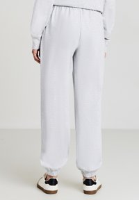 Graue Jogginghosen mit elastischem Bund, schmal zulaufenden Bündchen und weichem Material. Getragen mit weißen Sneakers mit schwarzen Akzenten.