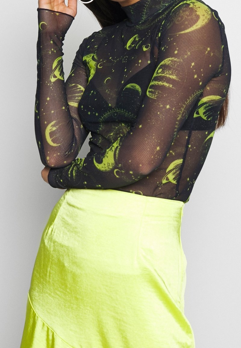 Musta verkkomallinen pitkähihainen paita, jossa on vihreitä taivaankappaleita. Yhdistetty korkeavyötäröiseen, kirkkaan keltaiseen hameeseen, jossa on teksturoitu pinta.