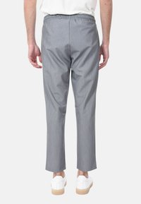 Pantaloni grigi in tessuto strutturato, con cintura elastica, gambe affusolate e lunghezza fino al polpaccio. Indossati con sneakers bianche.